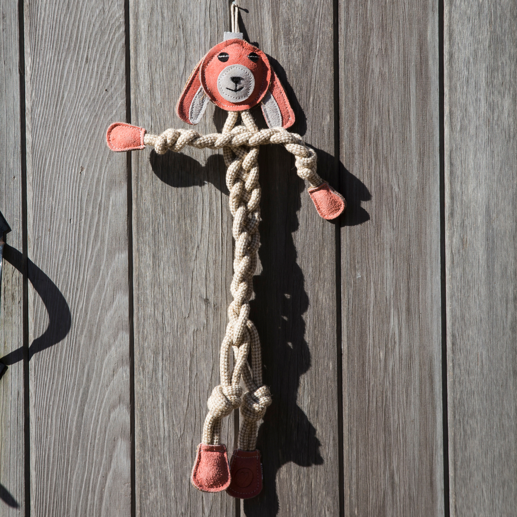 Lifestyle image of Bitsy the Bunny. Bitsy's handle above her head is supported by a nail to keep her hanging against the gray wooden fence.