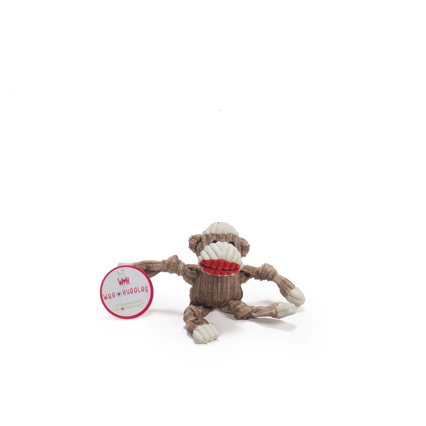 Image of the sock monkey looking at the camera. The top of the sock monkeys head is white with the fur on the face being light brown. The monkey has a white nose and red lips. The rest of the sock monkeys body has brown fur with the paws having white fur.
