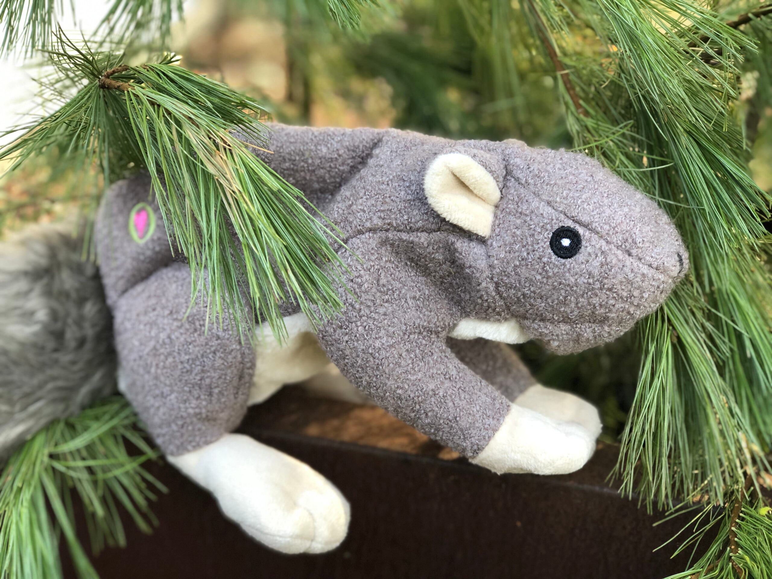 Lifestyle image of the large Feller Squirrel toy on a bench surrounded by tree sticks and leafs.