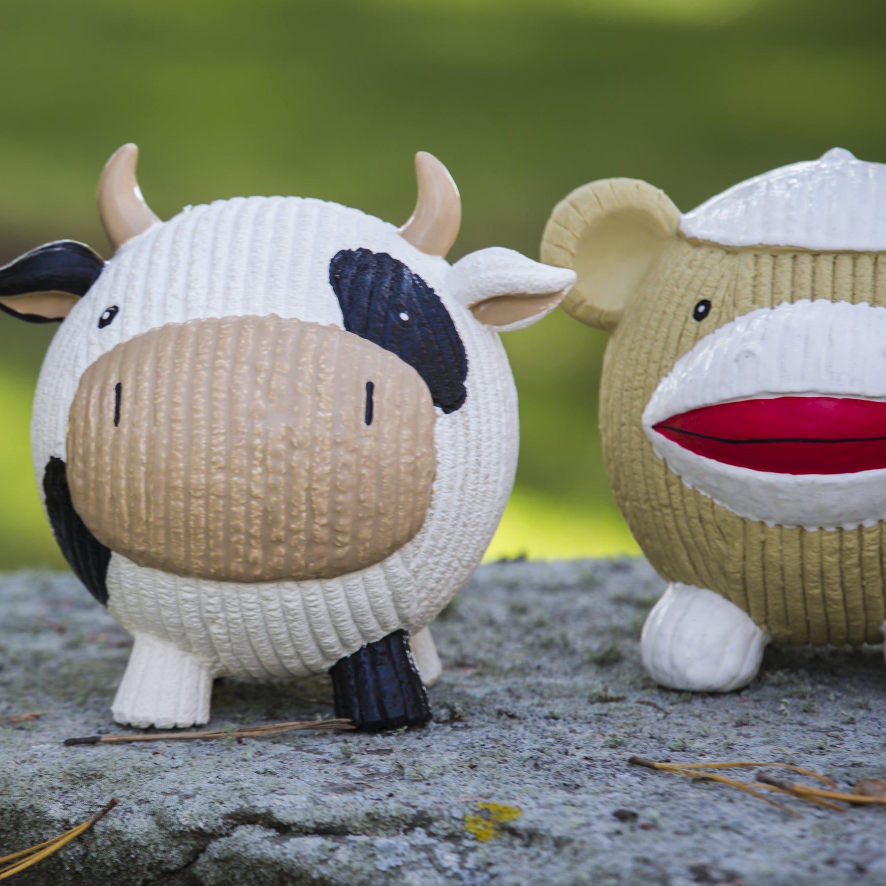Lifestyle Image of the Dottie cow. The cow is sitting on a rock slab. Next to the cow is the Ruff-Tex® Sock Monkey.