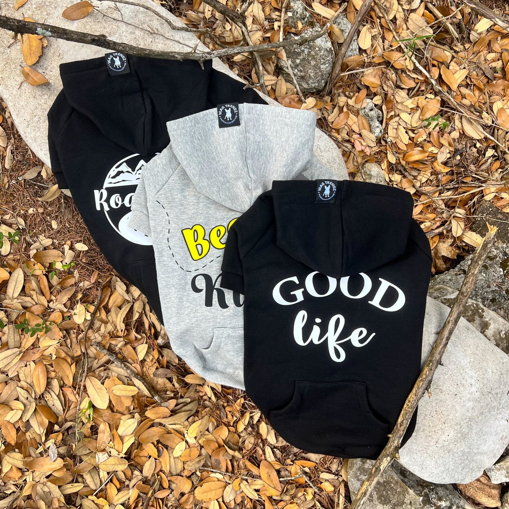 Hooded Sweatshirt For Dogs - "Good Life", "Bee Kind", and "Road Trip" hooded sweatshirts in black and gray - back view - outdoors laying on a log in a scenic fall background with brown leaves - Wag Trendz