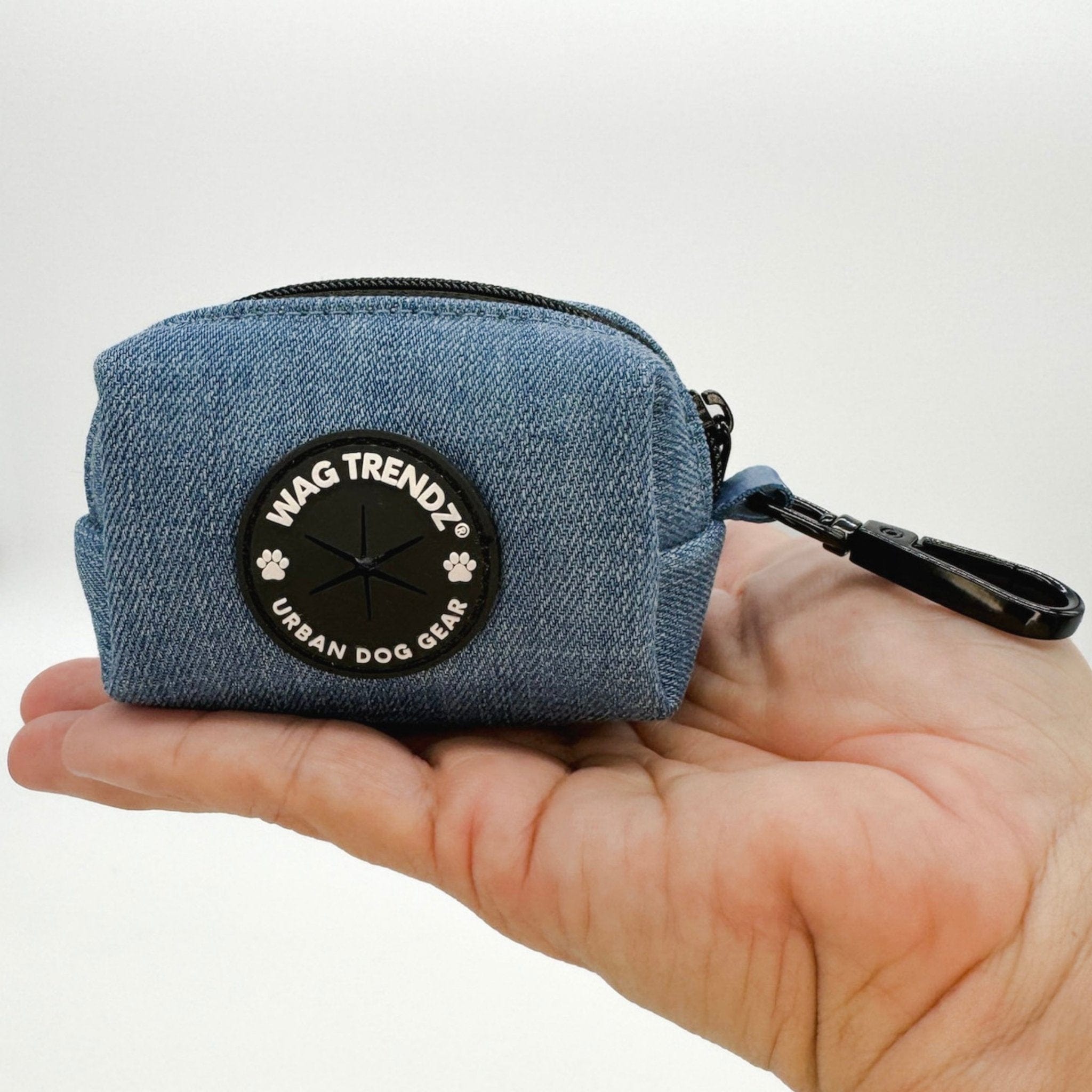 Dog Poop Bag Holder - Downtown Denim - blue jean with a black zipper and black rubber logo dispenser on front - sitting in the hand of a model against a solid white background - Wag Trendz