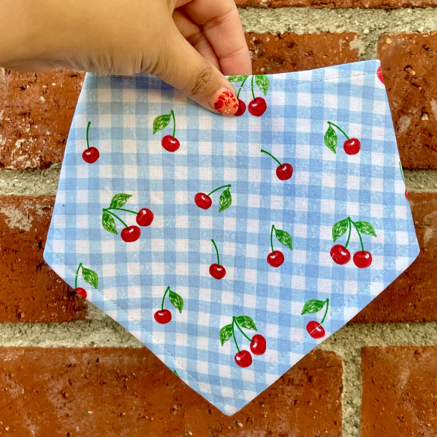 Cherry Jubilee handmade dog bandana featuring red cherries on blue-and-white gingham with an adjustable snap closure.